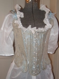 The stays are made of cotton brocade in tan and blue, with blue ribbon trim.